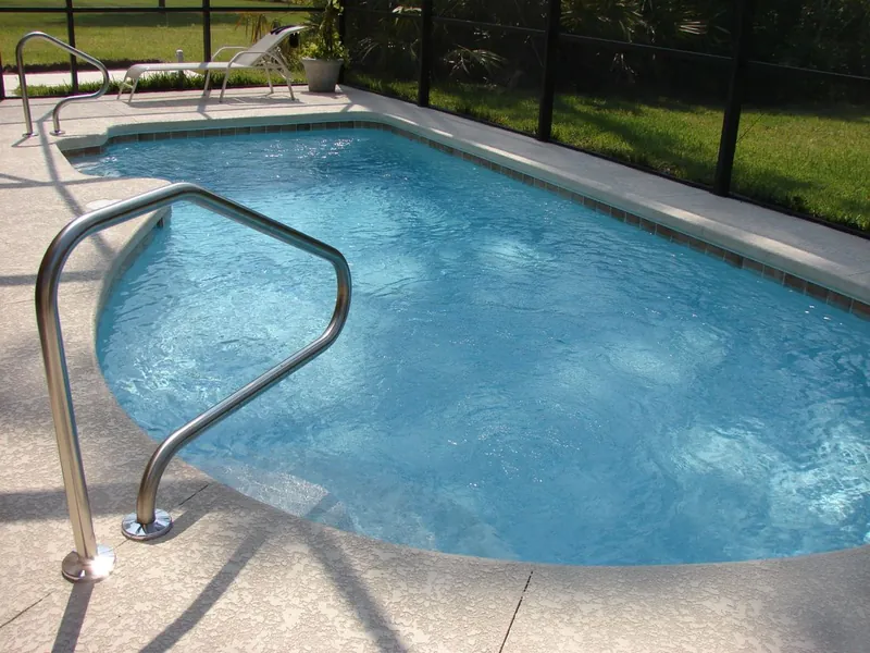 Clear blue pool with a stainless handrail and screened enclosure in San Marcos
