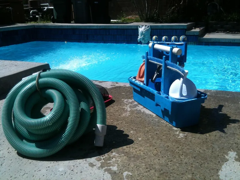 Pool vacuum hose and cleaning cart beside a clear backyard pool during weekly service